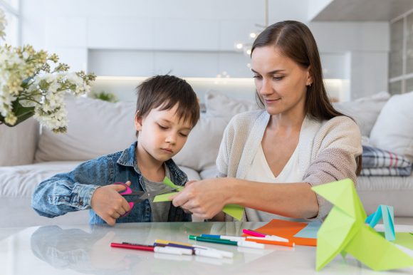 Mother and son cutting colored paper with scissors at home